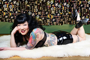 Portrait of Margaret Cho, star of the comedy concert film CHO DEPENDENT, with tattoos and latex skirt, lying on a a white lambskin