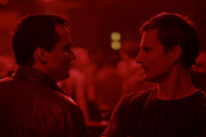 Filmstill PRAIA DO FUTURO von Karim Aïnouz, Clemens Schick und Wagner Moura stehen sich gegenüber in rotem Licht