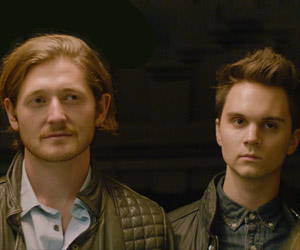 Film Still I LOVE YOU BOTH von und mit Doug Archibald; Andy (gespielt von Lucas Neff) und Donny (gespielt von Doug Archibald) stehen nebeneinander in Lederjacken vor der Tür