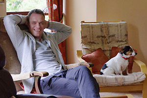 Film Still THE QUEEN OF IRELAND von Conor Horgan über die irische Drag-Queen Panti Bliss; der schwule Rory O'Neill sitzt ohne Drag, aber mit Hund in seinem Wohnzimmer