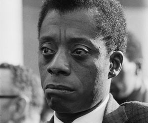 Film Still I AM NOT YOUR NEGRO von Raoul Peck und James Baldwin, erzählt von Samuel L. Jackson;  Autor James Baldwin sitzt mit ernstem Gesicht in einer Menschengruppe