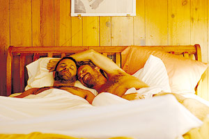 Film Still AUF DEN ZWEITEN BLICK – LAZY EYE von Tim Kirkman; Dean (gespielt von Lucas Near-Verbrugghe) und Alex (gespielt von Aaron Costa Ganis) liegen zusammen im Bett im sonnendurchfluteten Schlafzimmer
