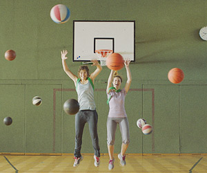 Film Still SIEBZEHN von Monja Art; Internatsschülerin Paula (gespielt von Elisabeth Wabitsch) und ihre Freundin Charlotte (gespielt von Anaelle Dézsy) springen in einer leeren Turnhalle in die Luft, während bunte Sportbälle um sie herum fliegen