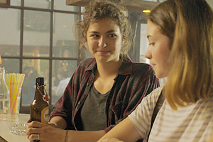 Film Still SIEBZEHN von Monja Art; Internatsschülerin Paula (gespielt von Elisabeth Wabitsch) steht an einem Kneipentresen mit Bierflasche neben ihrer Schulfreundin Charlotte (gespielt von Anaelle Dézsy), in die sie heimlich verliebt ist