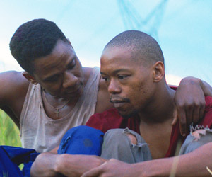 Film Still DIE WUNDE - THE WOUND - INXEBA von Regisseur John Trengove; Vija (gespielt von Bongile Mantsai) sitzt neben Xolani (gespielt von Nakhane Touré) und legt seinen Arm um ihn