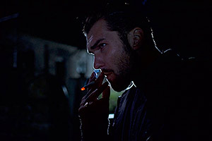 Film Still B&B BnB von Joe Ahearne mit Paul McGann; der Russe Alexie (gespielt von James Tratas) raucht in der Dunkelheit eine Zigarette, die sein Gesicht grimmig erhellt