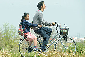 Film Still CLOSE-KNIT – Karera ga Honki de Amu toki wa von Naoko Ogigami mit Tôma Ikuta, Eiko Koike, Kenta Kiritani und Rin Kakihara; die 11-jährige Tomo (gespielt von Rin Kakihara) fährt auf dem Fahrradgepäckträger ihres Onkels Makio (gespielt von Kenta Kiritani) durch die japanische Kirschblüte