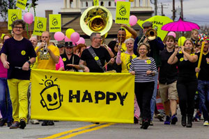 Film Still HAPPY: A SMALL FILM WITH A BIG SMILE von Michael Patrick McKinley über den Künstler Leonard Zimmerman alias Porkchop und seine Happy-Kampagne; eine Kampagnen-Parade mit auffälligem gelbem Banner und Blaskapelle zieht feierlich durch die Straßen