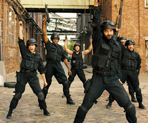 Film Still HARD WAY: THE ACTION MUSICAL von Daniel Vogelmann mit Oliver Tompsett, Hannah Britland, Charlie Anson; das SWAT-Sondereinsatz-Team B.E.A.T. steht mit hochgehaltenen Maschinengewehren in einem Industriekomplex