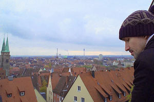 Film Still HOMØE: AUF DER SUCHE NACH GEBORGENHEIT von Bin Chen; der russische LSBT-Flüchtling Boris steht auf einem Balkon mit Blick über München