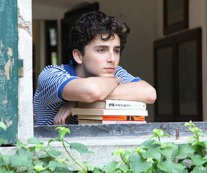 Film Still CALL ME BY YOUR NAME von Regisseur Luca Guadagnino; der Jugendliche Elio Perlman (gespielt von Timothée Chalamet) lehnt sich am offenen Fenster eines italienischen Landhauses auf einen Stapel Bücher