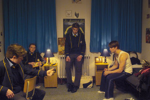 Film Still HANDSOME DEVIL von John Butler; Conor Masters (gespielt von Nicholas Galitzine) sitzt rechts auf seinem Bett, während seine Rugby-Freunde in Schuluniform zusammensitzen