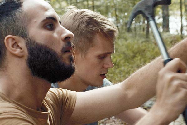 Film Still DIE HÜTTE AM SEE – A MOMENT IN THE REEDS, eine schwule Romanze zwischen einem Finnen und einem syrischen Flüchtling von Filmemacher Mikko Makela mit Janne Puustinen, Boodi Kabbani und Mika Melender; Leevi (gespielt von Janne Puustinen) arbeitet zusammen mit Tareq (Boodi Kabbani), der einen Hammer schwingt, an der Holz-Hütte