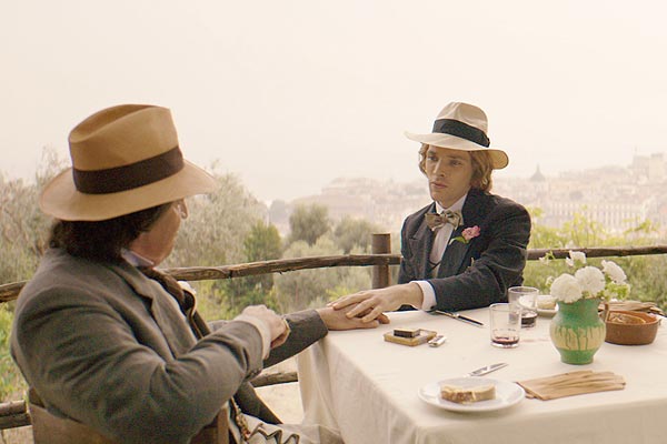 Film Still THE HAPPY PRINCE, Regiedebüt von Rupert Everett mit Colin Firth, Emily Watson, Tom Wilkinson und Béatrice Dalle; der homosexuelle Autor und Dandy Oscar Wilde (gespielt von Everett) hält die Hand des jungen Lords Alfred Bosie Douglas (gespielt von Colin Morgan) an einem gedeckten Tisch vor ländlicher Kulisse
