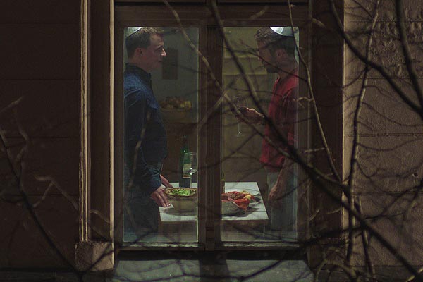 Film Poster THE CAKEMAKER – DER KUCHENMACHER – HaOfe MeBerlin – האופה מברלין von Regisseur und Autor Ofir Raul Graizer mit Sarah Adler und Zohar Shtrauss; Blick durch ein Fenster auf einen kleinen Küchentisch, an dem der israelische Geschäftsmann Oren (gespielt von Roy Miller) und der scheue deutsche Konditor Thomas (Tim Kalkhof) mit Kippa stehen