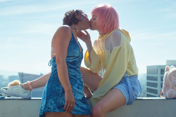 Film Still DADDY ISSUES von Regisseurin und Cutterin Amara Cash aus den USA, 2018; Maya Mitchell (gespielt von Madison Lawlor) und Jasmine Jones (gespielt von Montana Manning) küssen sich auf einem Balkon in einem Traum aus Neon-Gelb, -Pink und -Blau