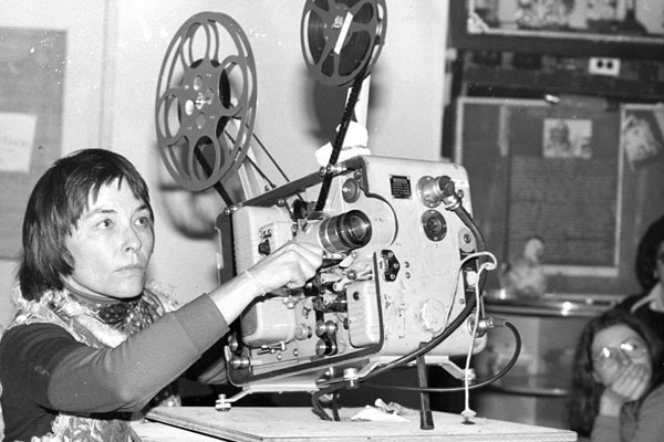 Film Still der lesbischen Doku DYKES, CAMERA, ACTION! von Regisseurin, Produzentin und Editorin Caroline Berler aus USA, 2018; ein altes Schwarz-Weiß-Bild von Filmemacherin Barbara Hammer, die einen 16-mm-Film vorführt